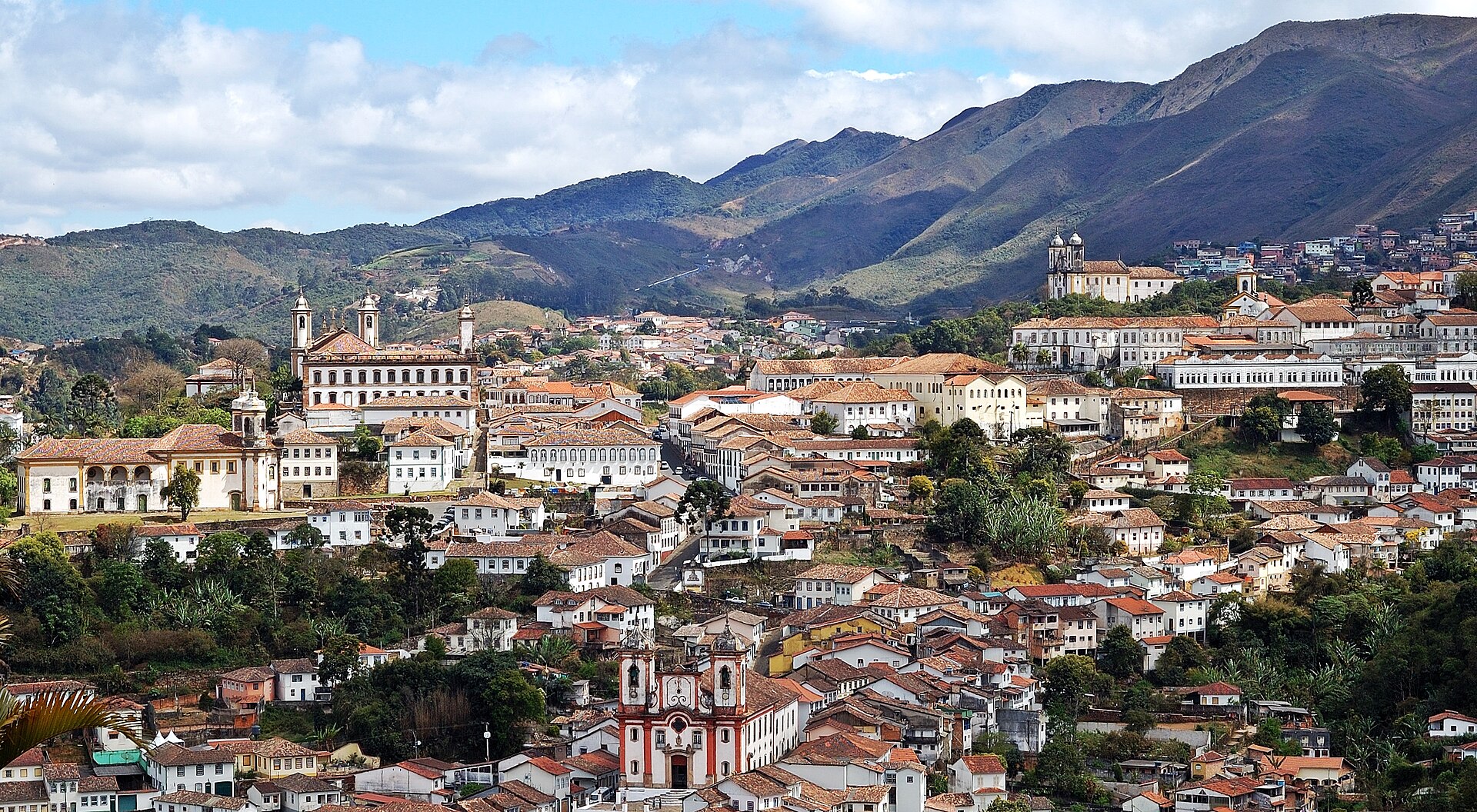 Panorama de Ouro Preto no vale: telhados de barro, igrejas barrocas e serras ao fundo.